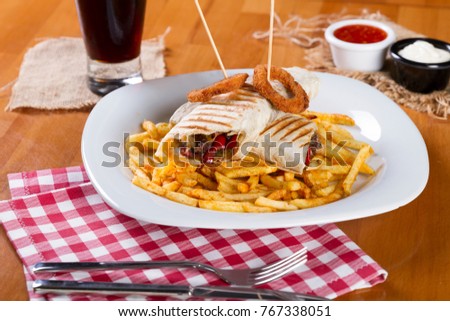 Delicious Turkish and Arabic Traditional Ramadan Tasty doner kebab with fresh salad trimmings and shaved roasted meat served in tortilla wraps on golden fried french fries, cola and wood background.