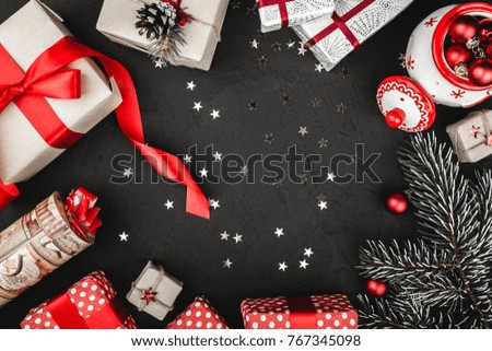 Upper top view of a red ribbon, Christmas presents, tree toys, sparkling stars  and evergreen branch on a stone black background, with space for text writing