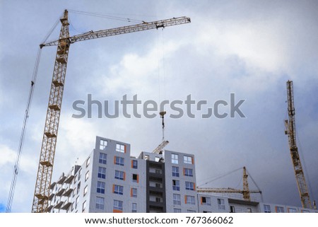 Working construction cranes and building under construction. Rainy cloudy sky