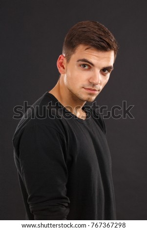 Portrait of a young guy with dark hair on a black background. Indoors.