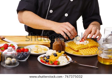 A close-up of the chef's hand imposes a strawberry on the waffles.