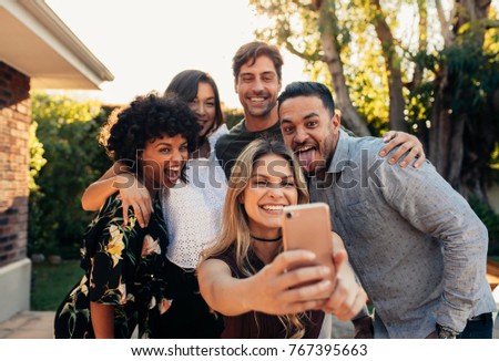Group of people partying together and taking selfie.  Young friends at housewarming party taking selfie with smart phone.