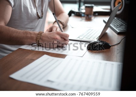 Close up of male hands drawing musical notes on paper. Man is sitting at desk near laptop