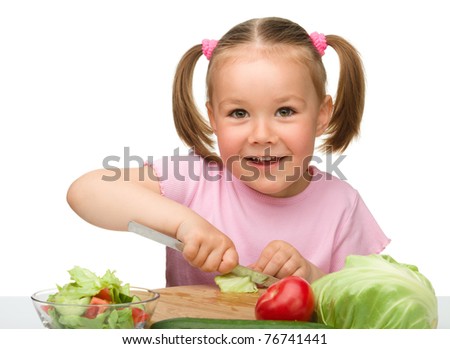 Little girl is cutting carrot for salad using kitchen knife, isolated over white