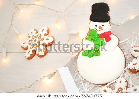 Christmas or new year gingerbread snowman and snowflakes in box on a white table with light garlands. Concept of gift. Picture for a confectionery catalog. Invitation or greeting card with copy space.