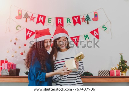 Young beautiful Asian woman give gift box to best women friend.Smiling face in room with Christmas tree decoration for holiday background.Christmas Party and celebration concept.