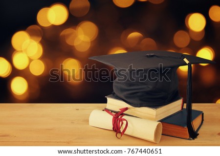 photo of graduation black hat over old books next to scroll diploma on wooden desk. Education and back to school concept