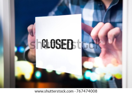 Bankruptcy, failed business going down or opening times concept. Man putting closed sign in window in cafe, restaurant, shop, store or agency. Late at night in city.