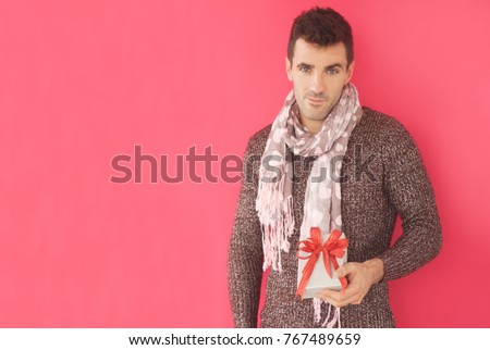 Handsome caucasian guy holding gift box standing in fron of pink background.