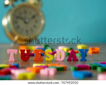 Colorful wooden word TUESDAY on wooden table and vintage alarm clock and background is powder blue. English alphabet made of wooden letter color.