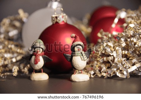 Cheerful penguins figurines with Santa hats and scarfs in front of red Christmas ornaments surrounded with  wrinkled gold decorative paper 