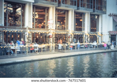 Blurred image of riverside restaurant in downtown San Antonio, Texas, USA. Riverfront popular dining places with colorful Christmas decoration along. People walking.