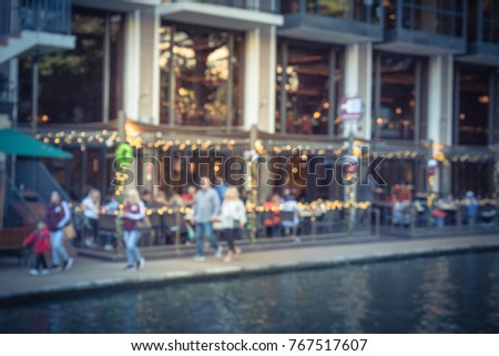 Blurred image of riverside restaurant in downtown San Antonio, Texas, USA. Riverfront popular dining places with colorful Christmas decoration along. People walking.