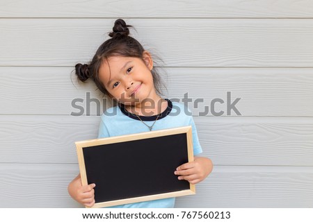 Portrait of a young Asian little girl holding a blank sign white blackboard on wood gray background