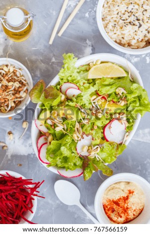 Green vegetable salad with rice, hummus and sprouts, gray background, top view. Healthy detox vegan food concept.