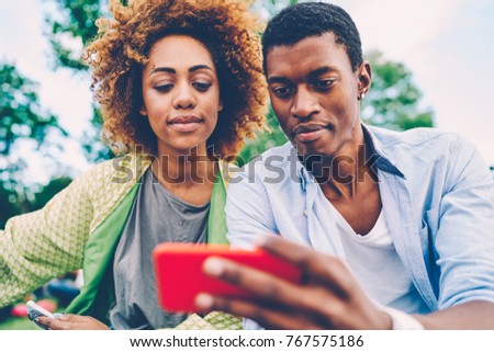 Cropped image of beautiful woman and handsome man taking togetherness selfie on smartphone camera and sharing made image with friends.Good looking afro american hipsters spending time outdoors