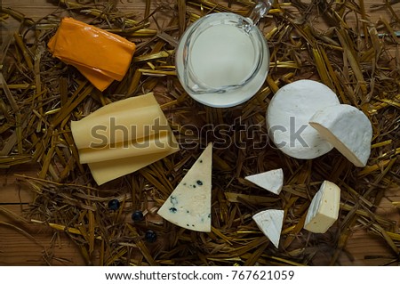 Cheeses and a glass jug with milk on the straw texture, the concept of rustic dairy products, free space for text