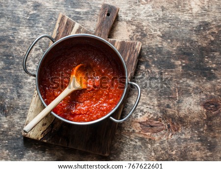 Classic homemade tomato sauce in the pan on a wooden chopping board on brown background, top view. Pasta, pizza tomato sauce. Vegetarian food  Royalty-Free Stock Photo #767622601
