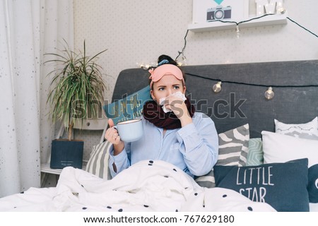 Young sick woman in bed with flu and cold blowing her nose and drinking hot tea. Seasonal influenza concept Royalty-Free Stock Photo #767629180