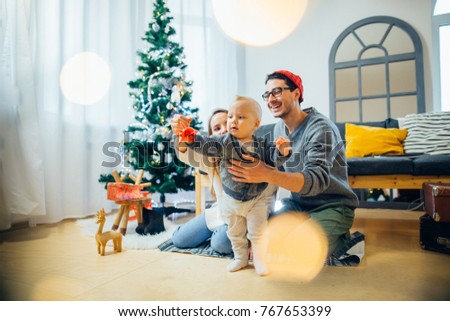 Happy mother and father showing Christmas ball to baby near Christmas tree