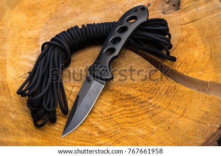 The folding knife is black and the parachute cord. Wooden background.