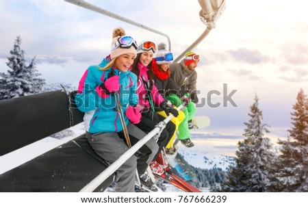 group of cheerful friends are lifting on ski-lift for skiing in the mountains