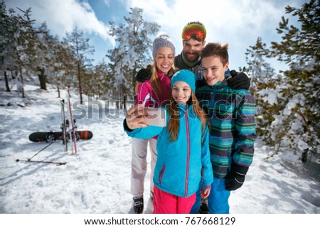 Happy family smiling and making selfie with mobile on winter ski vacation