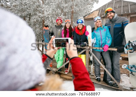 girl taking pictures of cheerful friends on cold holidays winter day