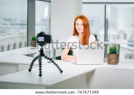 Young woman recording video on camera mounted on tripod for her vlog