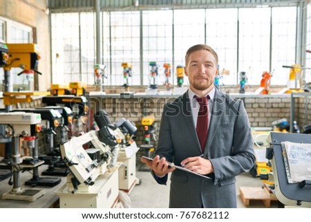 Portrait of successful sales assistant wearing suit posing smiling confidently at camera, standing in showroom selling industrial machine tools