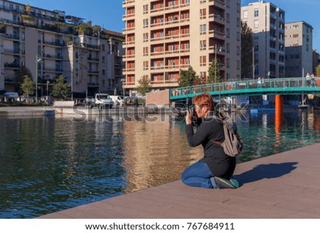 A female photographer takes a photo with a digital camera on a canal in Milan.