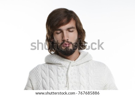 Isolated headshot of handsome unshaven young European man keeping eyes closed, having calm expression in his hairy face while meditating at home, relaxing mind after hard working day at office
