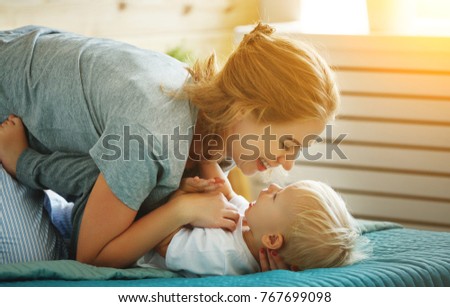 happy family mother and baby son toddler laughing and hugging in bed
