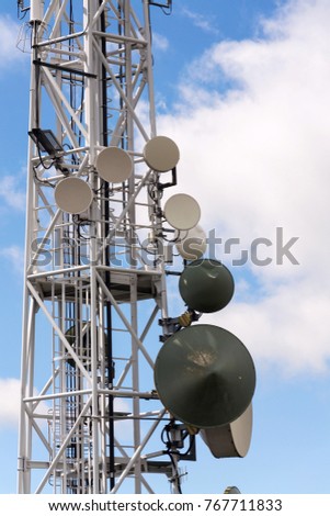 Transmitters and aerials on telecommunication tower with cloudy blue sky background, digital communication and encryption safety concept