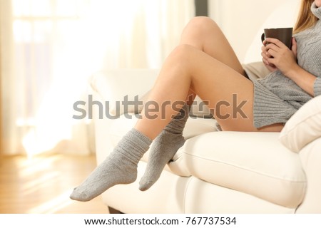 Detail of a beautiful woman legs in winter sitting on a sofa in the living room in a house interior