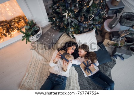 Merry Christmas and Happy Holidays. Cheerful mom and her cute daughter girl exchanging gifts. Parent and little child having fun near Christmas tree indoors. Loving family with presents in room.