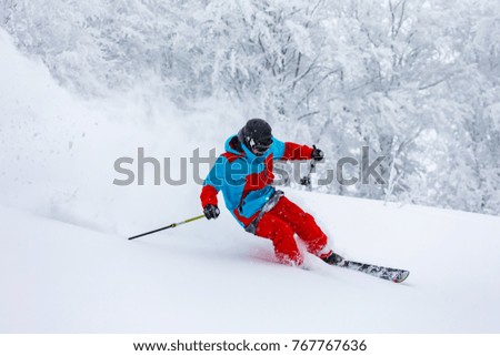 A skier is riding downhill in the deep snow. Winter season, good powder day.