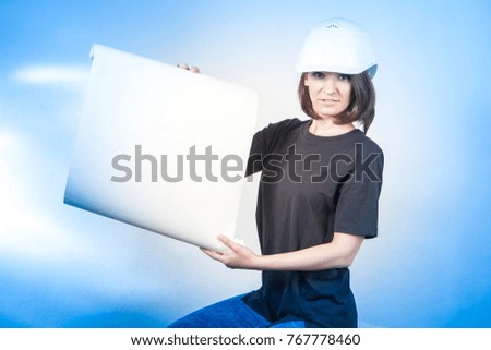 Girl in a construction helmet. A girl builder holds a white sheet. Building.