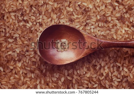 A small portion of rice in a wooden spoon on the background texture of the rice. Red rice with a wooden spoon close up.