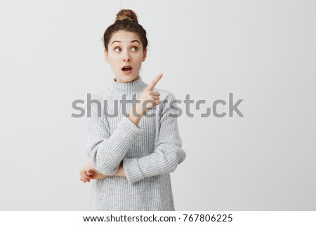 Teenage girl with wonder looking to side and showing with index finger. Curious female employee trying to pay attention over white background. Attention concept Royalty-Free Stock Photo #767806225