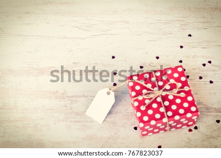 Empty note tied over a red dotted gift box. Wooden background. Vintage style.