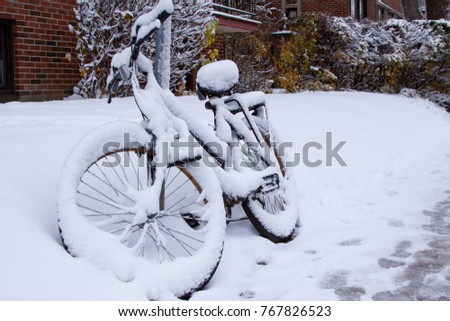 Angled front view of a bicycle covered in freshly fallen snow, locked to a sign pole on a street in Montreal, QC, on a bright November day.