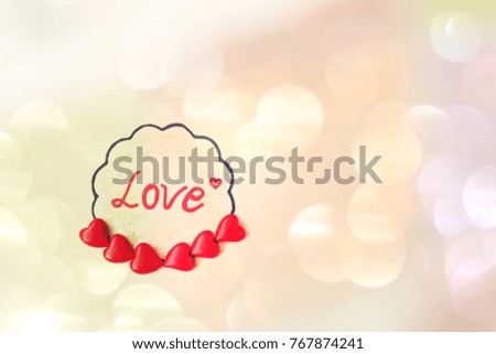 Top View of cute paper note "Love" with mini red hearts on multi color bokeh background. Pastel color. Can use for Medicine, Candy ,Valentine's , Wedding , Happy Birthday, banner, print. Copy space.