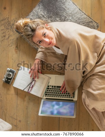 Young beautiful woman in the living room lying on the floor and communicates with friends over the computer, covered with a blanket for the cold. Top view