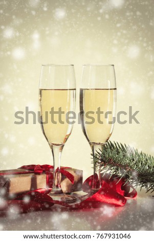 The concept of Christmas. Two glasses with champagne, a gift and a fur-tree branch. Snowfall.
