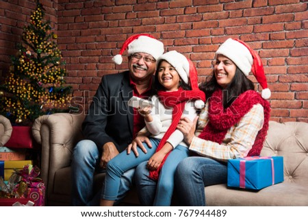 indian grandparents and grand daughter celebrating christmas while watching television and clicking selfie