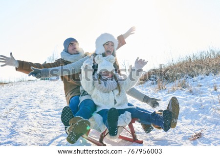 Family with parents and daughter playing toboggan in winter with enthusiasm