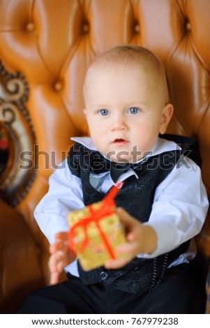 beautiful baby sitting in a chair with a gift in hands
