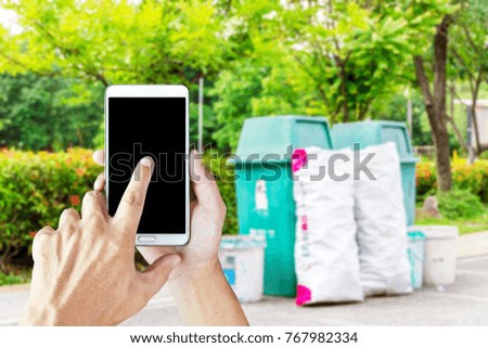 Man use mobile phone, blur image of trash placed in the park as background.