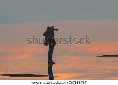 Silhouette of alone woman takes a picture of a sunset reflected in waters of salt lake, Ankara